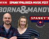 Two smiling hosts stand in front of a promotional banner for Spanky’s Music Fest, featuring the Spanky’s logo and 102.9 The Hog branding (Waterford, WI).