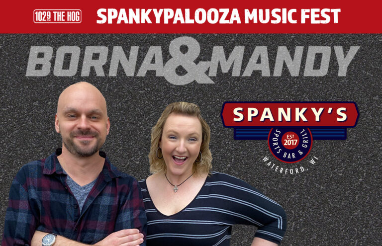 Two smiling hosts stand in front of a promotional banner for Spanky’s Music Fest, featuring the Spanky’s logo and 102.9 The Hog branding (Waterford, WI).