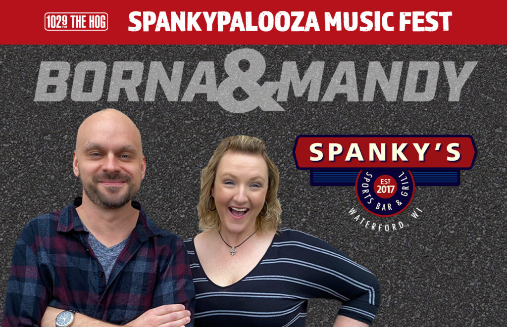 Two smiling hosts stand in front of a promotional banner for Spanky’s Music Fest, featuring the Spanky’s logo and 102.9 The Hog branding (Waterford, WI).