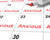 Close-up of a calendar with red 'Anxious' text in several date boxes and a marker near date 16, suggesting recurring anxiety.