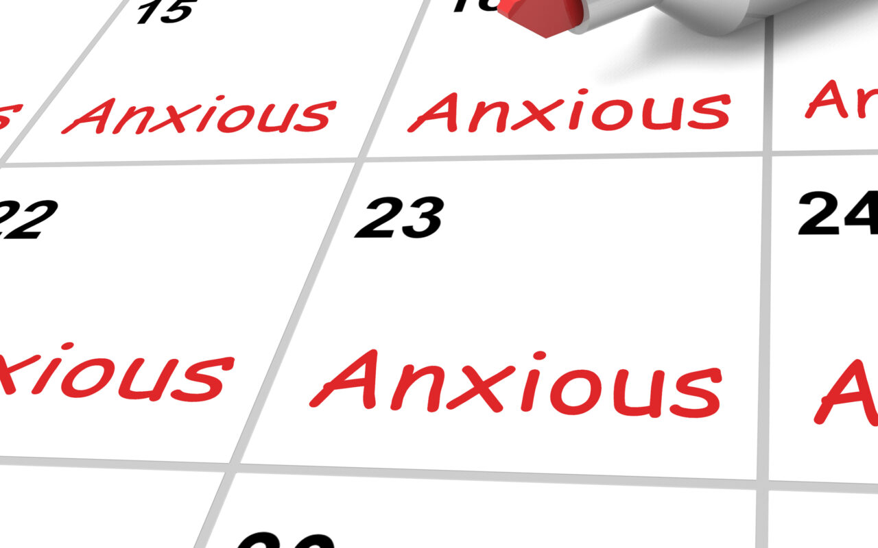 Close-up of a calendar with red 'Anxious' text in several date boxes and a marker near date 16, suggesting recurring anxiety.