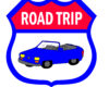 Shield-shaped sign with a blue convertible and a red banner that reads ROAD TRIP, indicating travel theme.