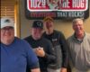 Four men posing in a radio studio under a sign that reads '1029 FM The Hog' and 'Everything that rocks!'