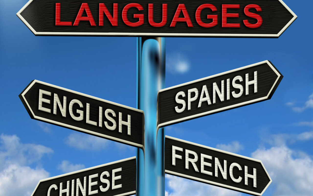 Signpost with arrows labeled LANGUAGES and English, Spanish, Chinese, and French against a blue sky.